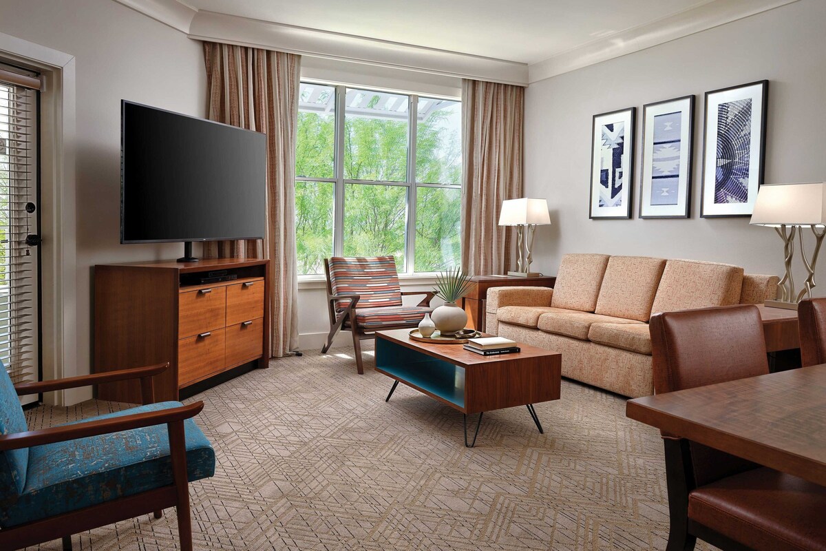 A modern living room with a flat-screen TV, a sofa, a coffee table, and a dining table.