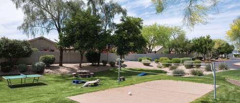 Un espacio exterior cuidado con mesa de ping-pong, red de voleibol y una pequeña estatua.