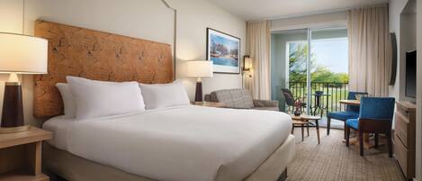 A hotel room with a large bed, a desk with a chair, a TV, and a balcony with a view.
