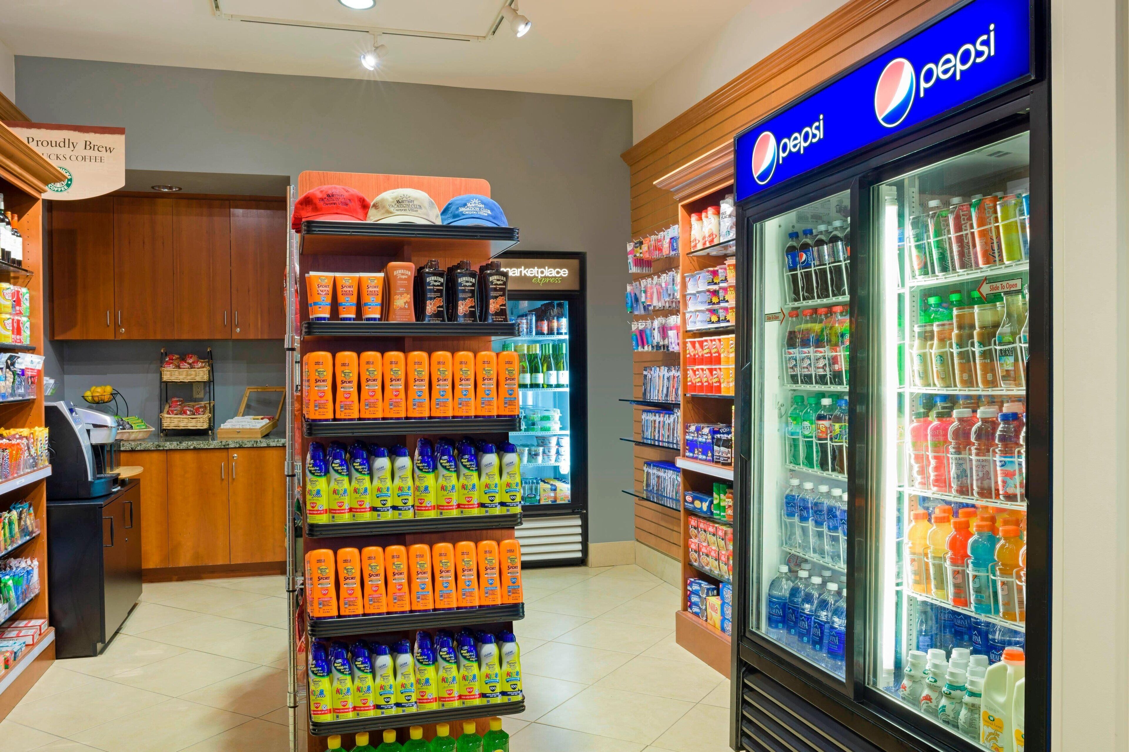 Une épicerie dont les rayons sont remplis de divers produits, avec une machine à café et un réfrigérateur à boissons de la marque Pepsi.