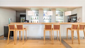 Eine Bar mit einer langen Theke, mehreren Flaschenregalen und vier Holzstühlen.
