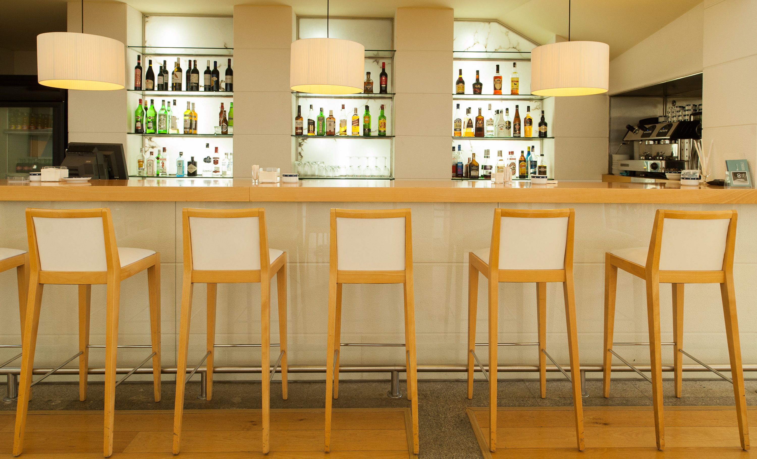 A bar area with wooden chairs, a counter with various bottles, and a coffee machine.