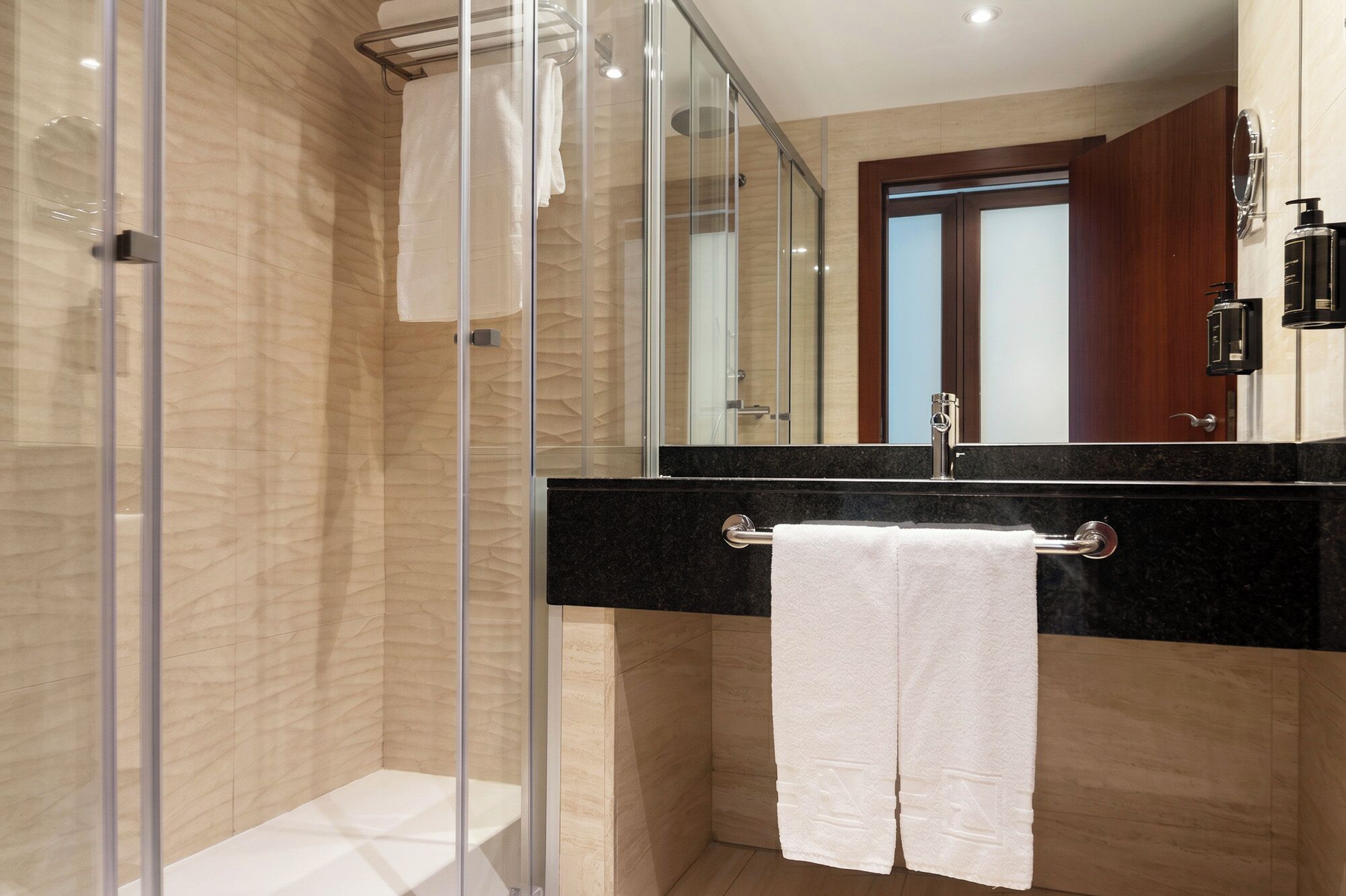 A modern bathroom with a glass shower enclosure, a black countertop sink, and a white towel hanging on a metal rack.