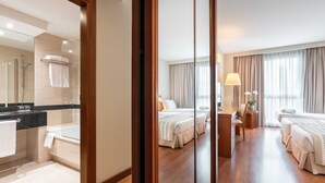 Ein Hotelzimmer mit einem großen Spiegel, einer Badewanne, einem Schreibtisch, zwei Betten und einem fensterbepflanzten Fenster.
