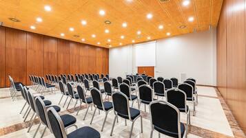 A conference room with rows of chairs, a projector screen, and a wooden ceiling with recessed lighting.