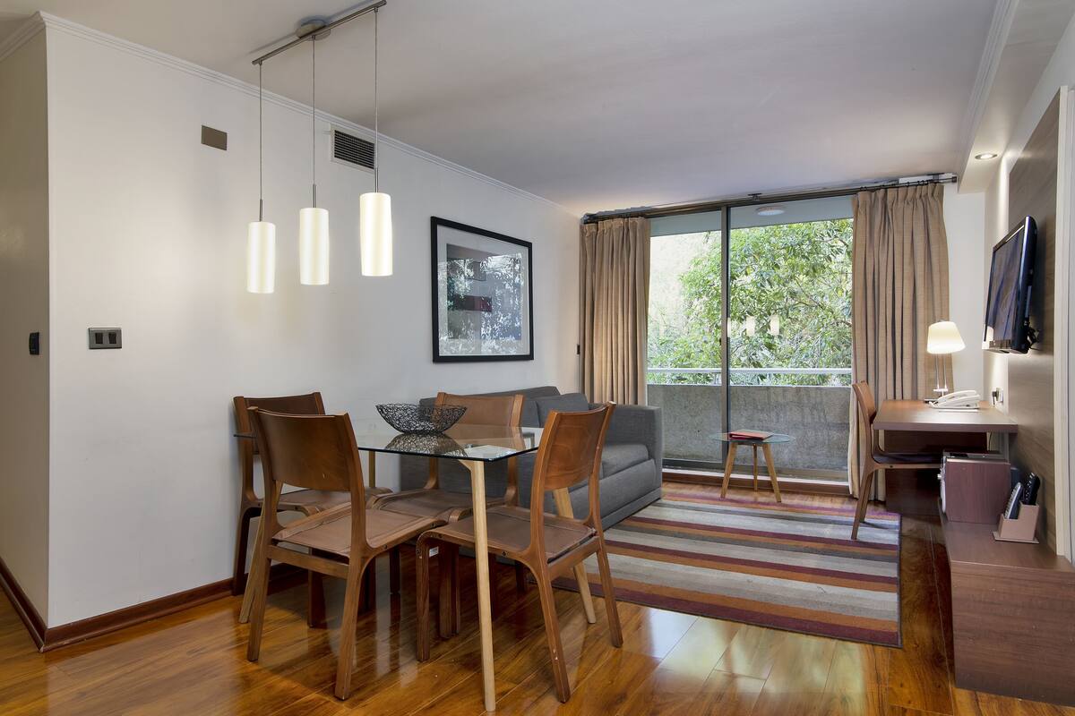 Una sala de estar moderna con comedor, sofá, televisor y balcón con cortinas.