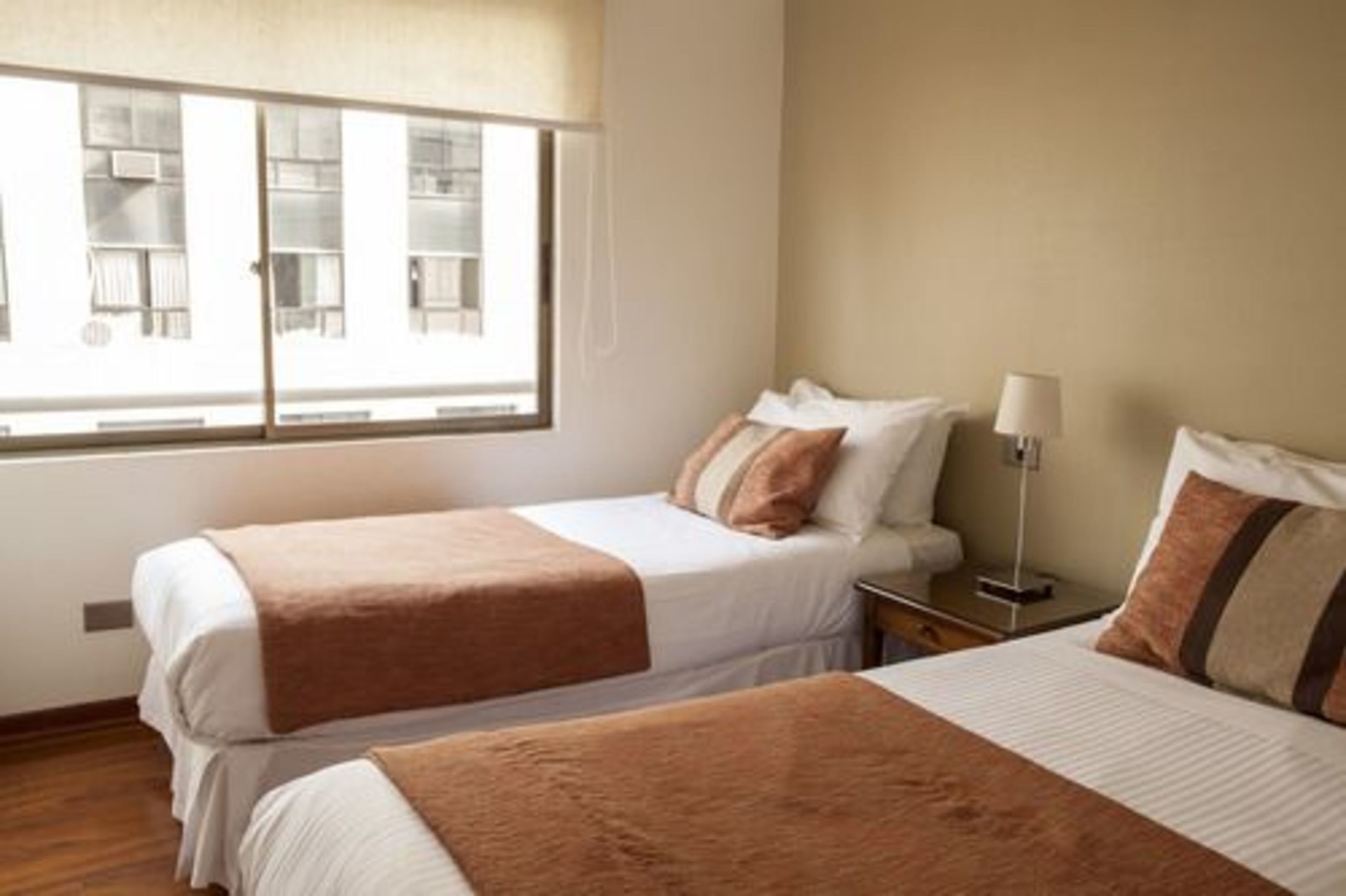 Habitación de hotel con dos camas, una mesita de noche, una lámpara y ventana con vista a un edificio.
