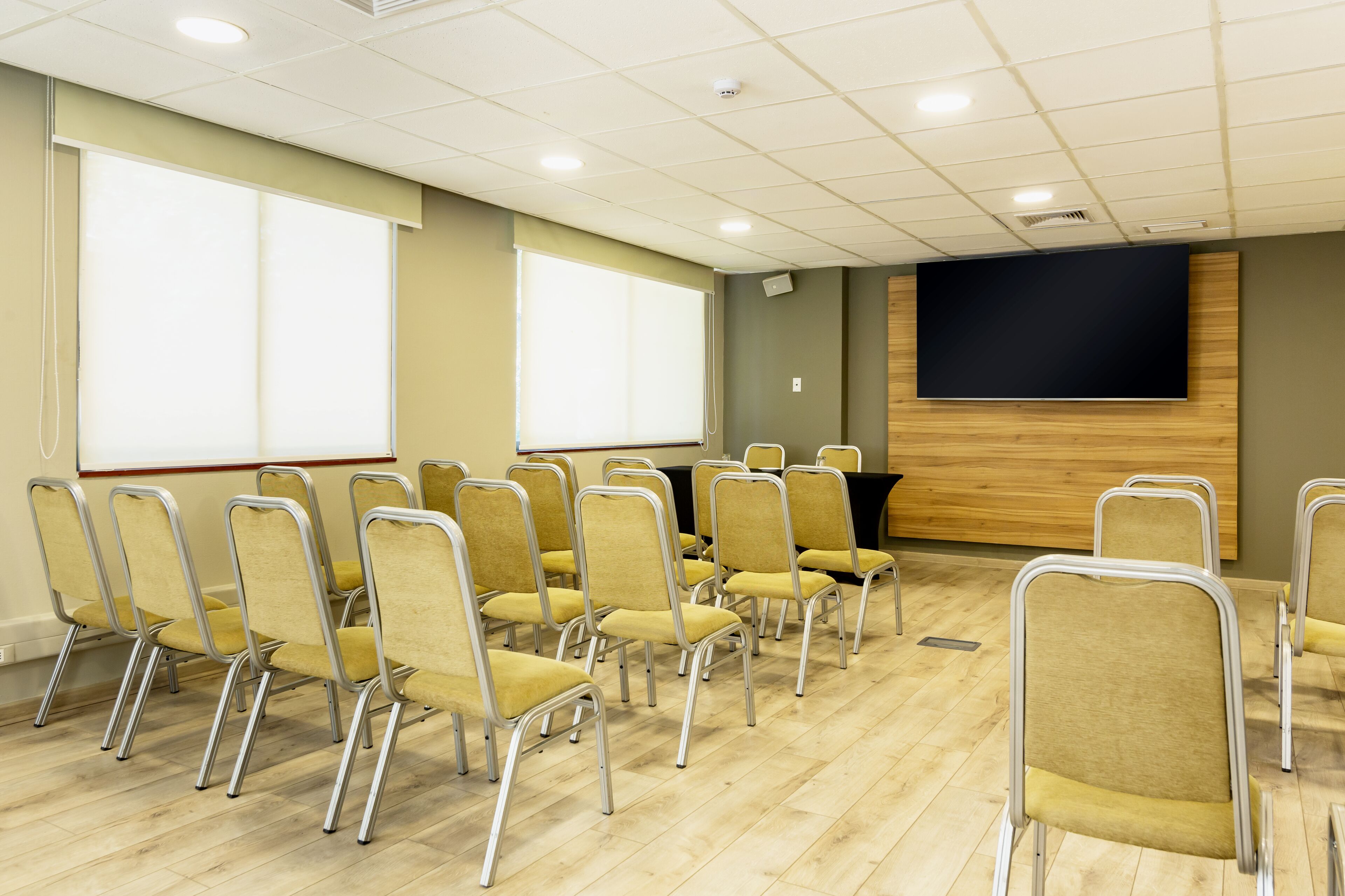 Une salle de conférence avec des rangées de chaises jaunes, un grand écran et un mur recouvert de panneaux en bois.