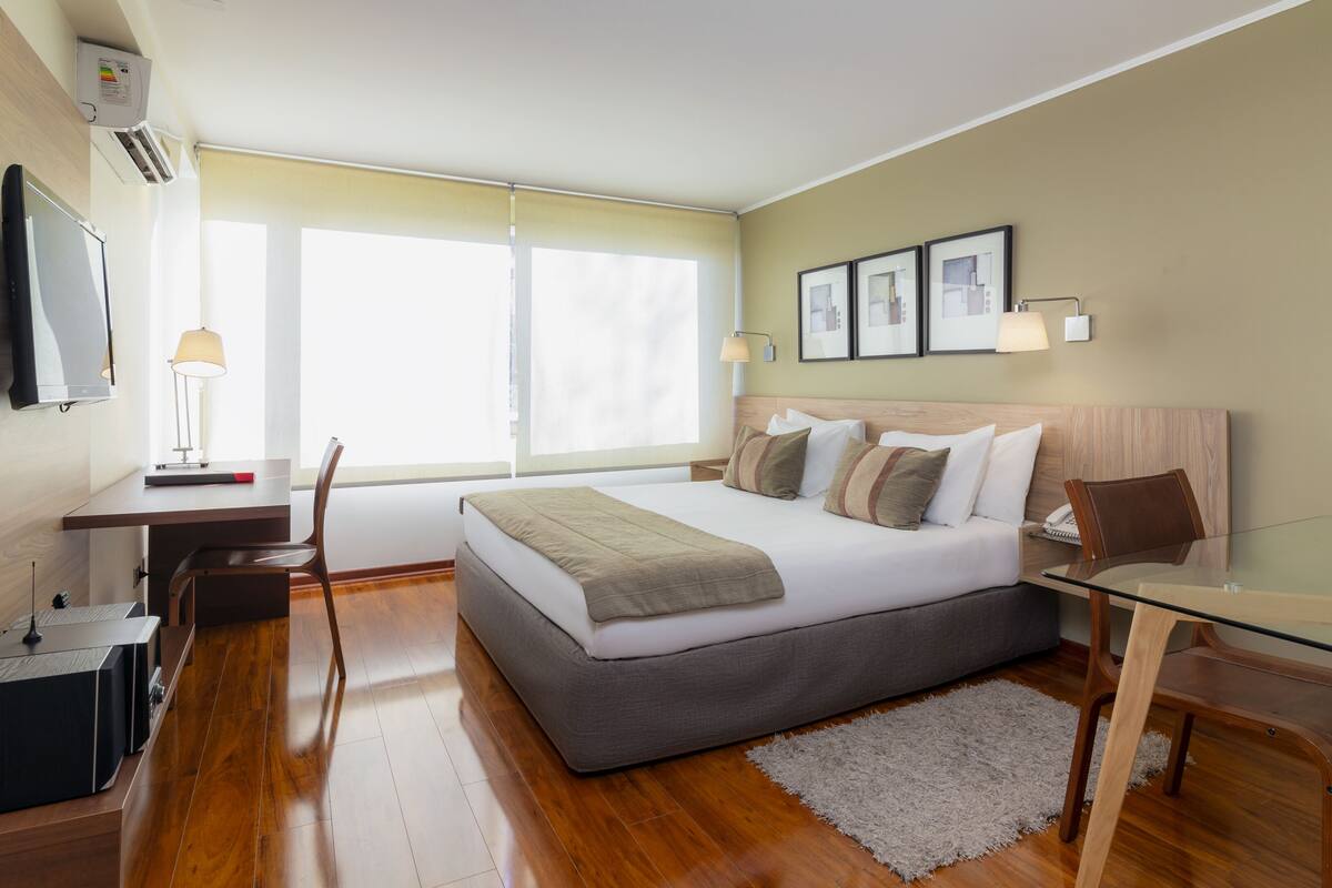 Una habitación de hotel moderna con una cama grande, un escritorio, una silla, un televisor y una mesita de cristal.