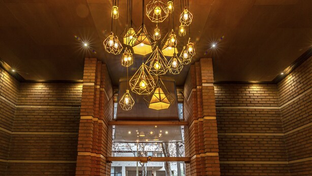 A lobby with a wooden ceiling, brick walls, and a geometric chandelier. - Time Suite - Comfort Apartments (Santiago)