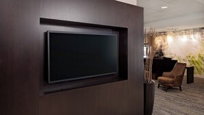 A modern interior with a large flat-screen TV mounted on a dark wall, a brown leather chair, and a patterned carpet. - Courtyard Fort Worth I-30 West Near Naval Air Station-JRB (Fort Worth)