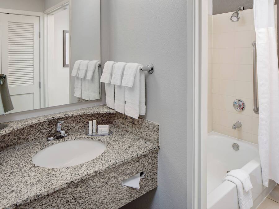 A bathroom with a granite countertop sink, a mirror, two white towels, and a bathtub with a shower curtain.