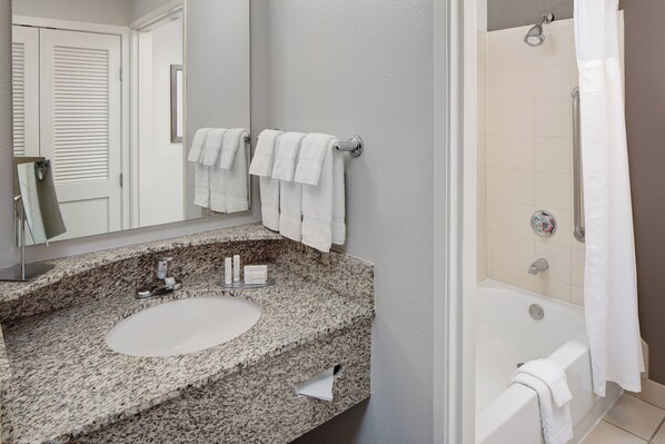 A bathroom with a granite countertop sink, a mirror, two white towels, and a bathtub with a shower curtain.
