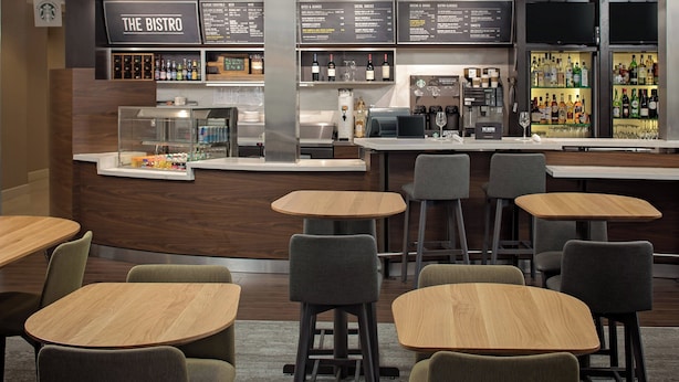 A modern bistro with wooden tables and chairs, a bar area with a menu, and a variety of bottles and glasses on display. - Courtyard Fort Worth I-30 West Near Naval Air Station-JRB (Fort Worth)