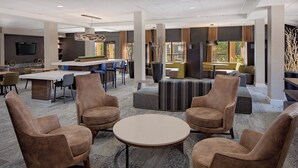 A modern lounge area with leather armchairs, a round table, and a bar area with stools. - Courtyard Fort Worth I-30 West Near Naval Air Station-JRB (Fort Worth)