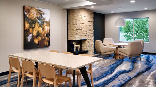 A modern conference room with a stone accent wall, a fireplace, and a large window with a view of trees. - Fairfield Inn and Suites by Marriott Yakima (Yakima)