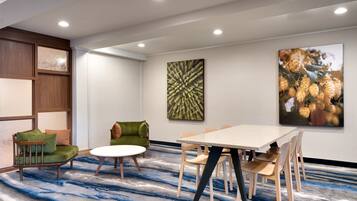 A modern meeting room with a round table, green and beige chairs, and a blue patterned carpet.