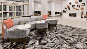 A modern living room with a sectional sofa, round tables, and a patterned rug. - Hilton Garden Inn Birmingham/Lakeshore Drive (Birmingham)