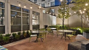 An outdoor patio with round tables and chairs, string lights, and potted plants. - Hilton Garden Inn Birmingham/Lakeshore Drive (Birmingham)
