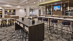 A modern hotel lobby with a central dining area, a bar, and a kitchen. - Hilton Garden Inn Birmingham/Lakeshore Drive (Birmingham)