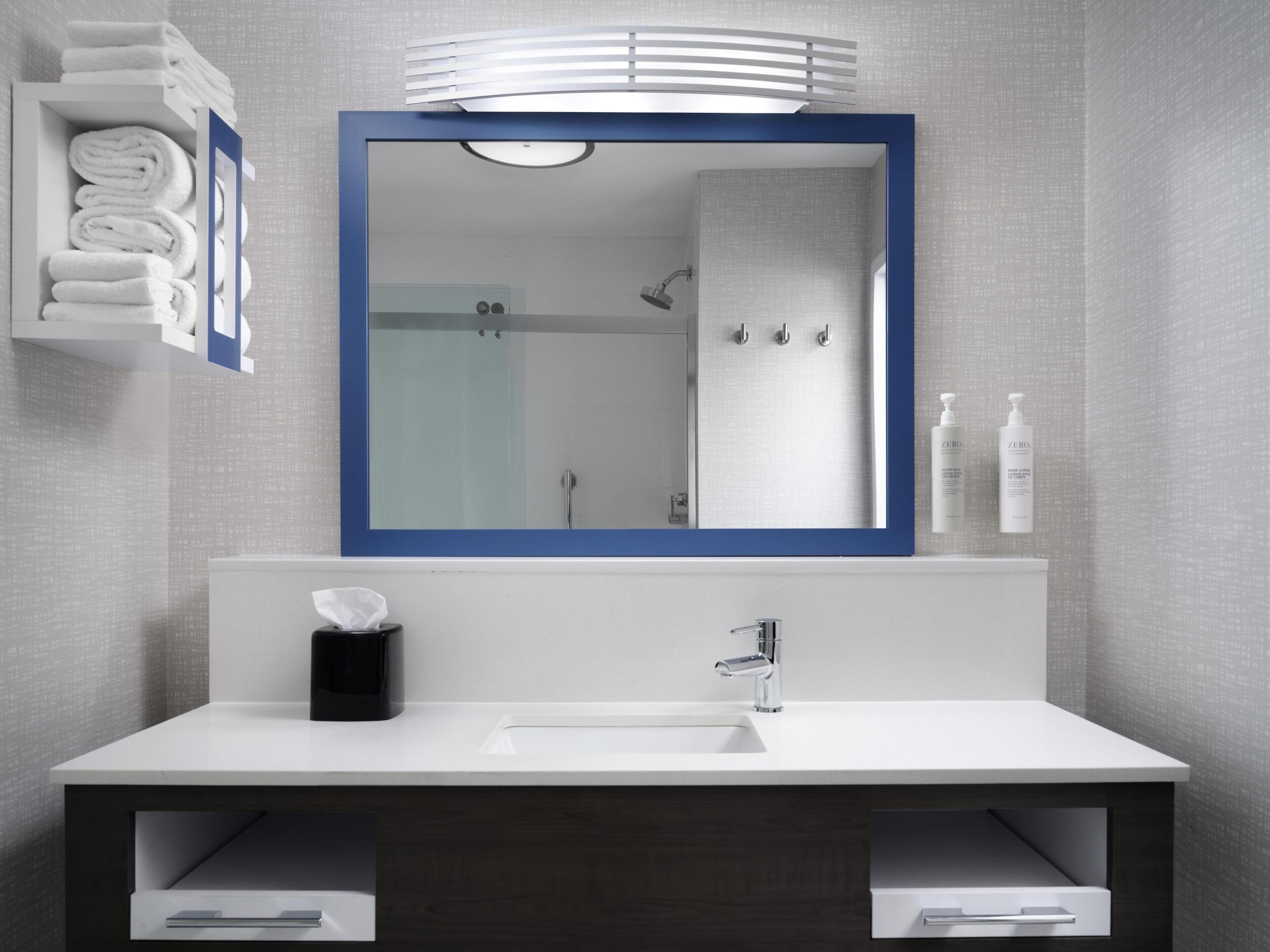 A modern bathroom with a large mirror, a white sink, a towel rack, and a shower area.