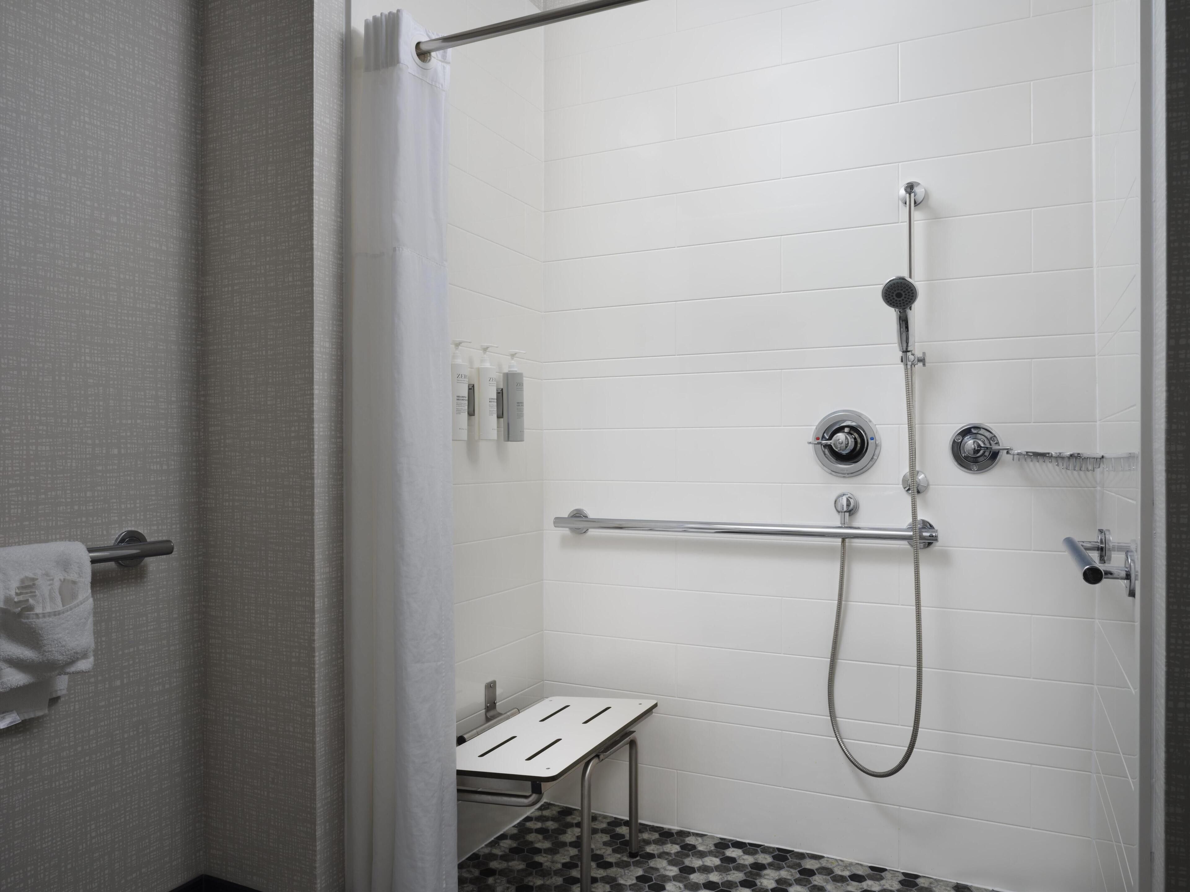 A shower with a handheld showerhead, a wall-mounted faucet, and a handheld showerhead.