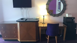 A hotel room with a flat-screen TV mounted on the wall, a desk with a lamp, a chair, a dresser, and a microwave. - Scottish Inns Albany (Albany)
