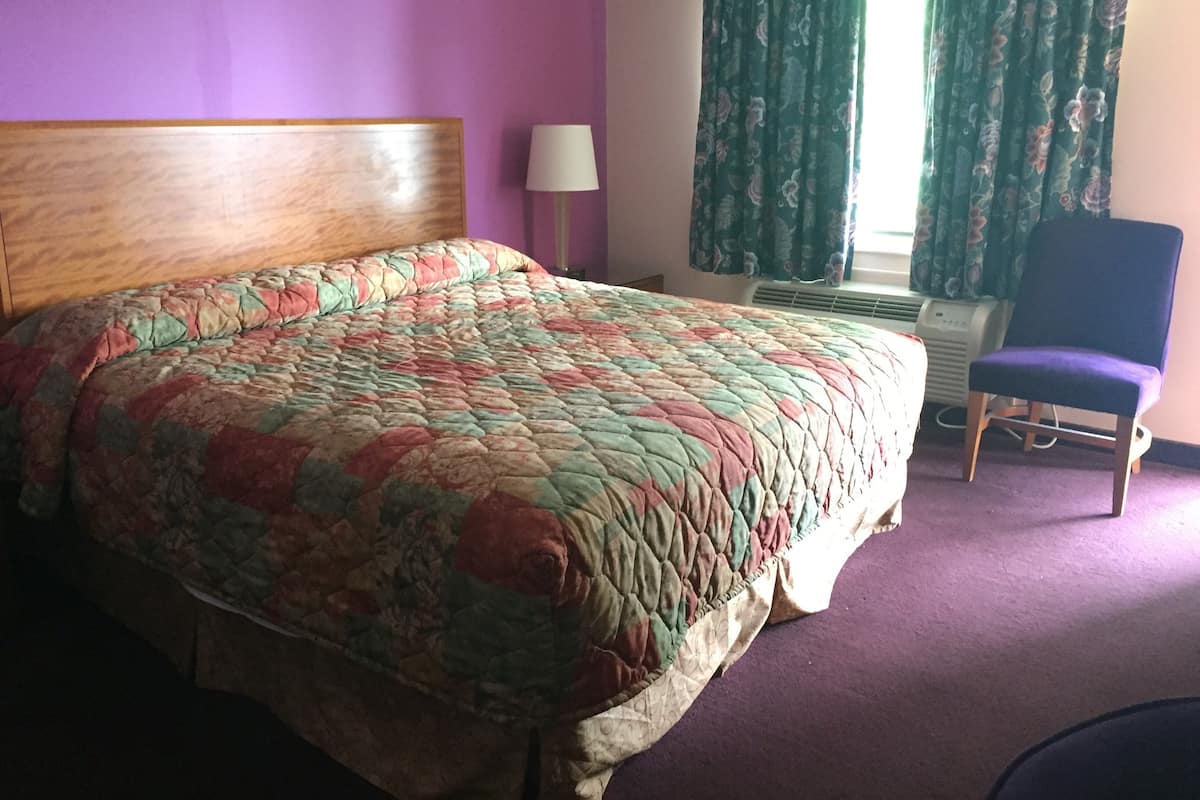 A bed with a floral quilt, a chair, a lamp, and a window with curtains.