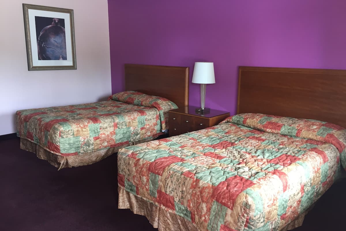 A hotel room with two single beds, a wooden headboard, a bedside table with a lamp, and a framed picture on the wall.