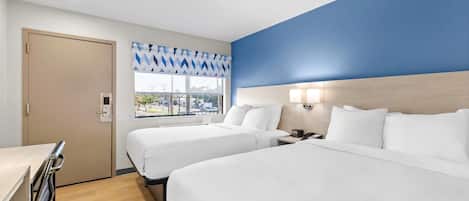 Habitación de hotel con dos camas, un escritorio, un ventanal con vista a la calle y una pared azul de acento.