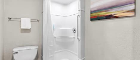A bathroom with a white toilet, a shower enclosure, and a painting on the wall.