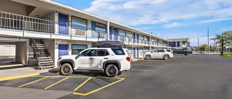 A parking lot with a row of single-story buildings, each with a balcony and a door.