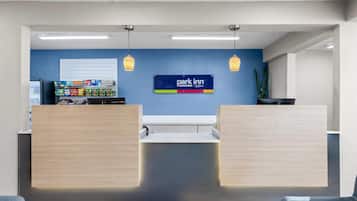 Una zona de recepción con pared azul, un letrero de 'Park Inn' y un bar de aperitivos con diversos productos envasados.