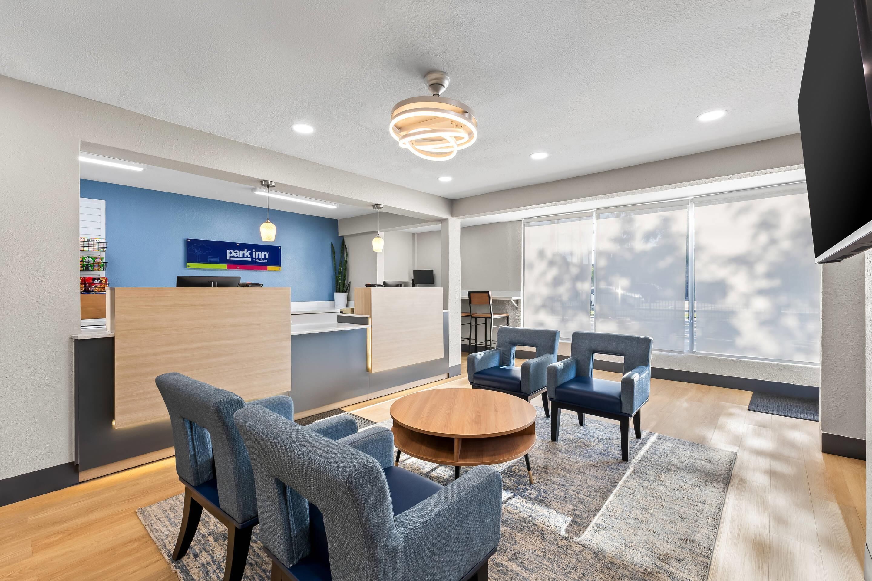 Een moderne hotellobby met een receptiebalie, een zithoek en grote ramen.