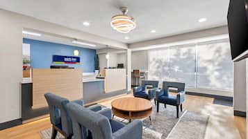 Een moderne hotellobby met een receptiebalie, een zithoek en grote ramen.