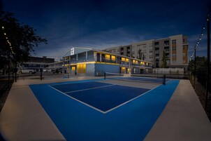 Un edificio de varios pisos con área de piscina, estacionamiento y una calle con autos.