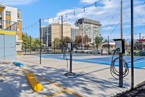 Zona de carga para vehículos eléctricos al aire libre, con cielo despejado, edificios modernos al fondo y un espacio de estacionamiento azul.