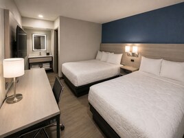 Habitación de hotel con dos camas, un escritorio, un espejo y un baño visible al fondo.