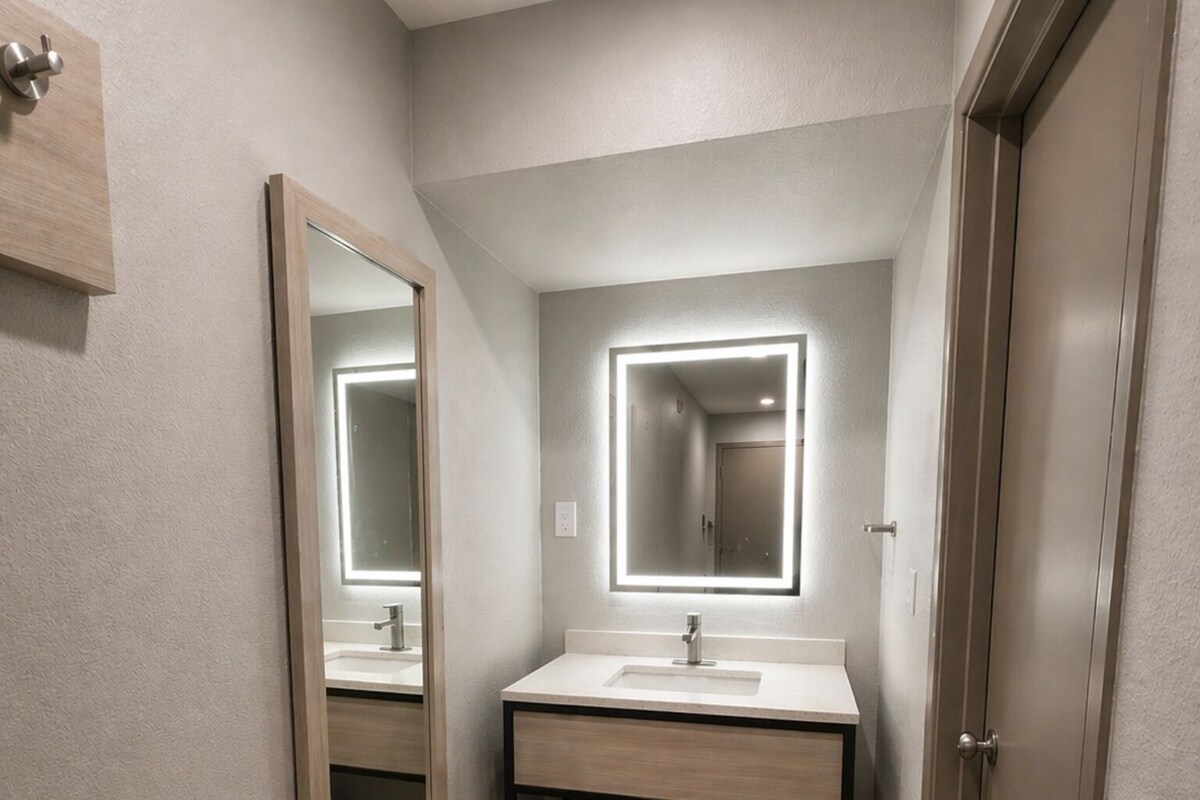 A modern bathroom with a vanity, a large mirror, and a bench.