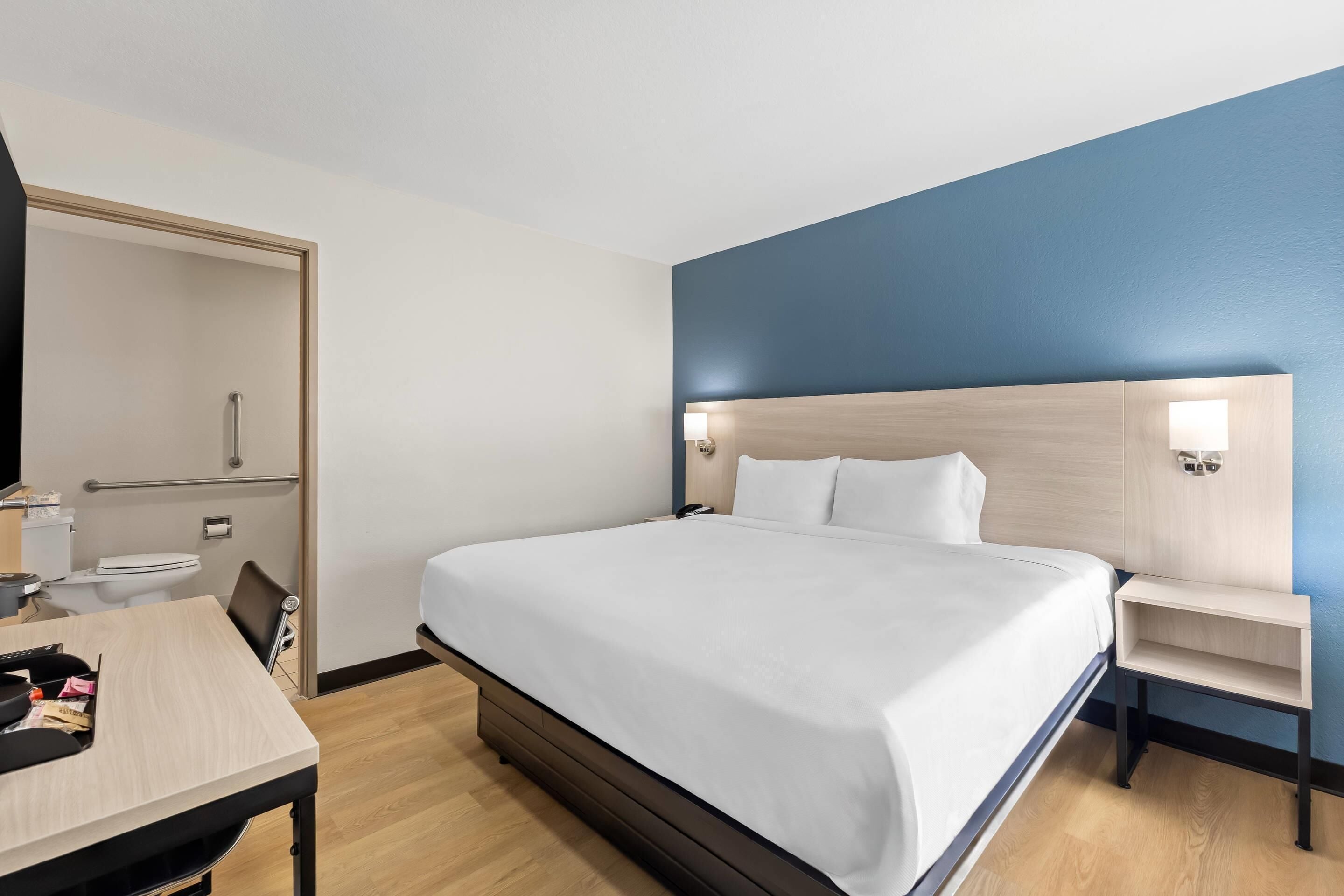 Une chambre d’hôtel comprenant un lit, une table de chevet, un bureau avec une chaise, des toilettes et un miroir.
