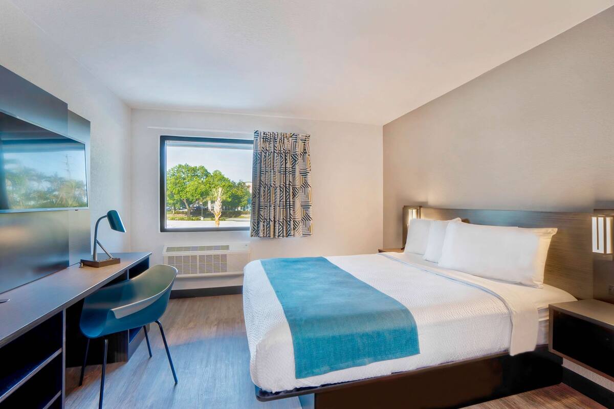 Een moderne hotelkamer met een groot bed, een bureau, een stoel en een raam met uitzicht op bomen.