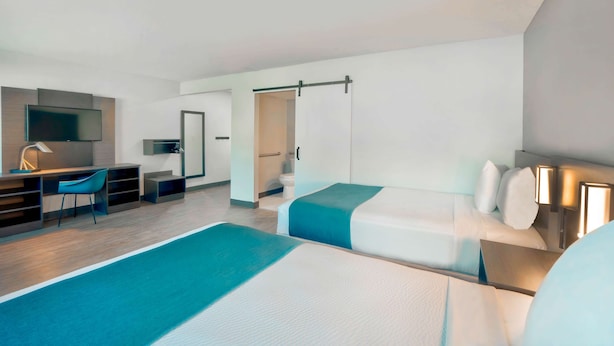 A modern hotel room with two beds, a desk, a chair, and a TV. - Motel 6 Fort Lauderdale, FL (Fort Lauderdale)