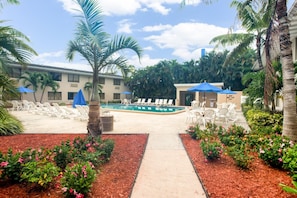 A pool area with lounge chairs, a palm tree, and a building in the background. - Motel 6 Fort Lauderdale, FL (Fort Lauderdale)