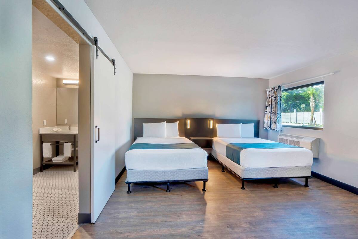 Een hotelkamer met twee bedden, een badkamer en een raam met gordijnen.