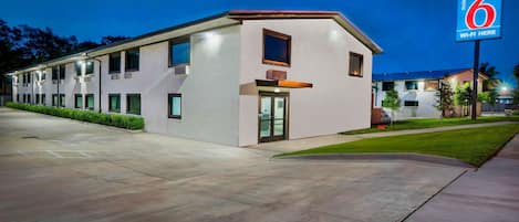 Un motel au design moderne, caractérisé par un toit plat, de grandes fenêtres et un panneau indiquant la présence d’une connexion Wi-Fi.