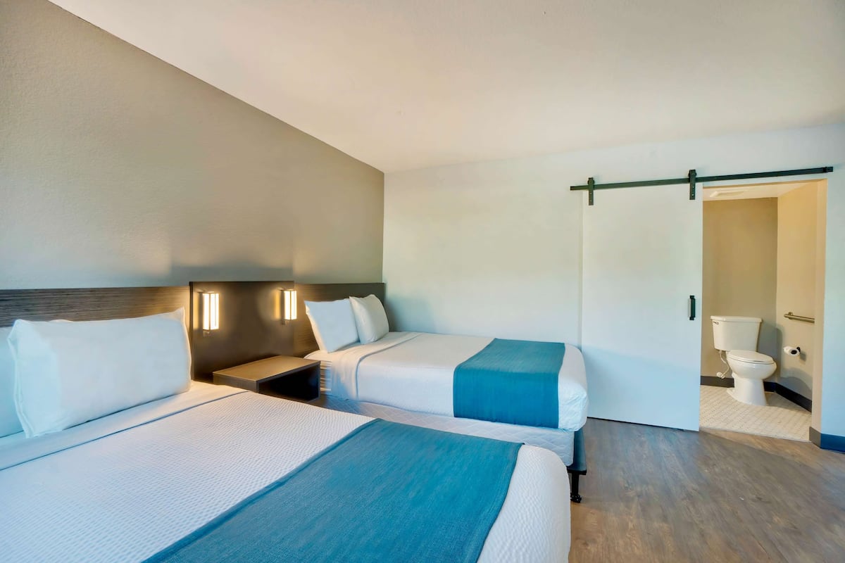 Een hotelkamer met twee bedden, een nachtkastje, een wandlamp en een schuifdeur naar een badkamer.