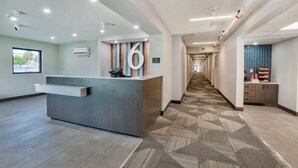 A hotel reception area with a modern design, including a reception desk, a large number '6' sign, and a patterned carpet. - Motel 6 Fort Lauderdale, FL (Fort Lauderdale)