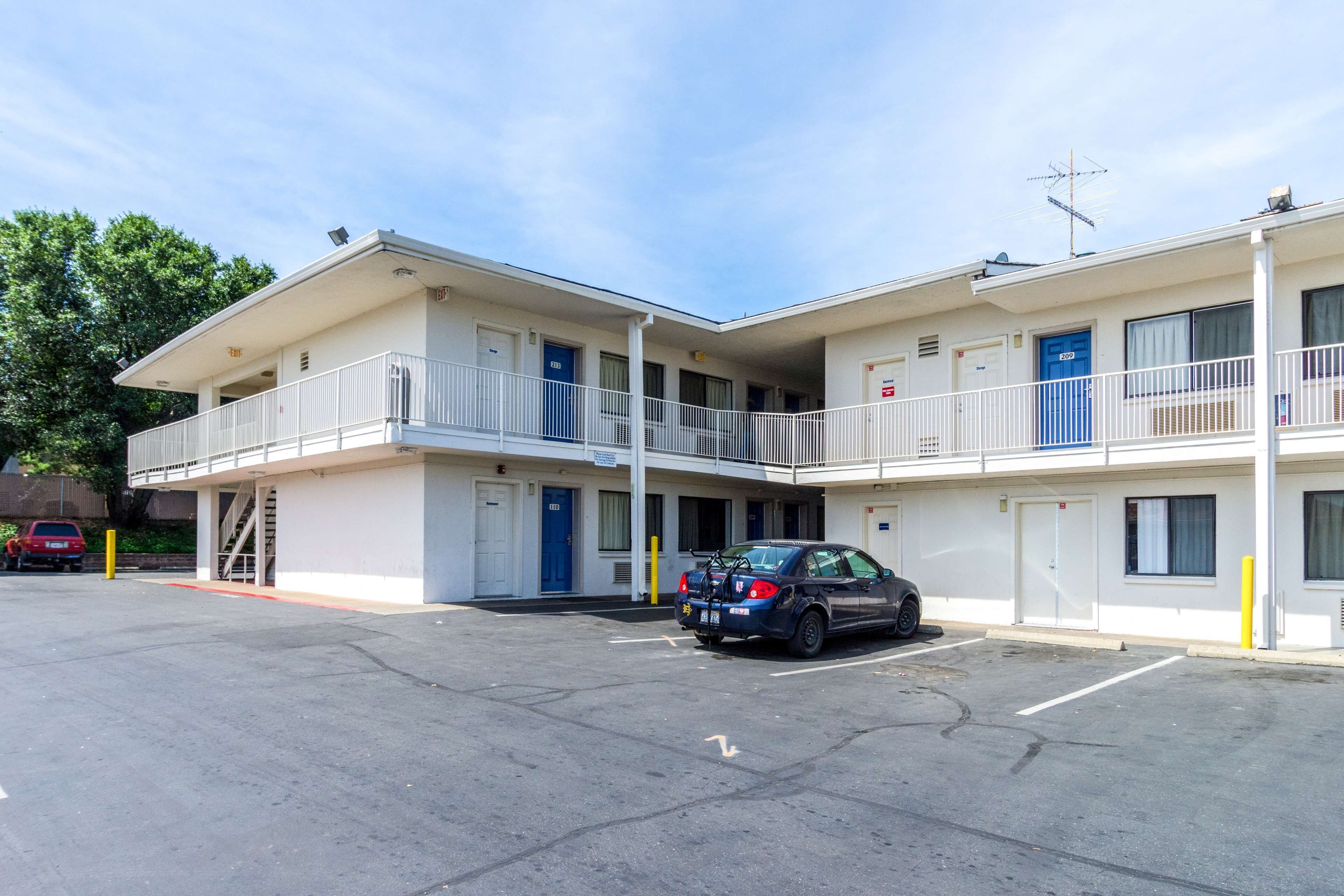 A motel with two-story buildings, a parking lot, and a car parked in front.