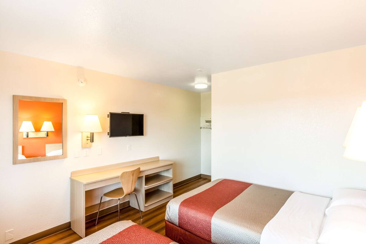 A hotel room with two beds, a desk, a chair, a TV, and a mirror.