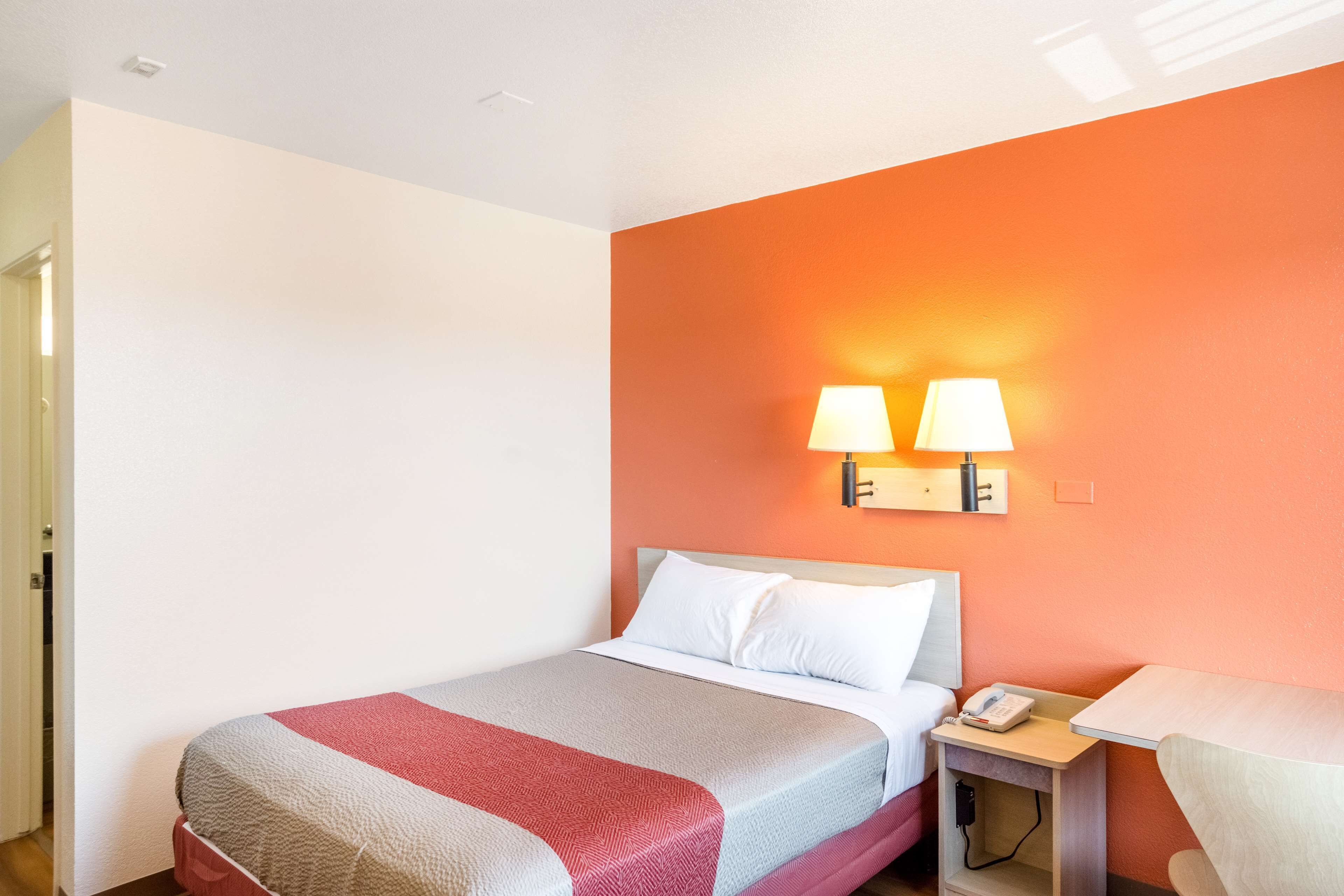 A hotel room with a bed, a nightstand with a lamp, and a chair.